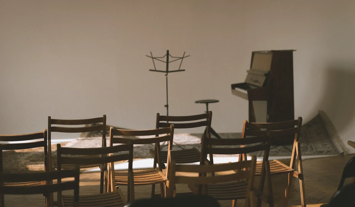 An empty music room with wooden chairs, a piano, and a sheet music stand ready for a performance.