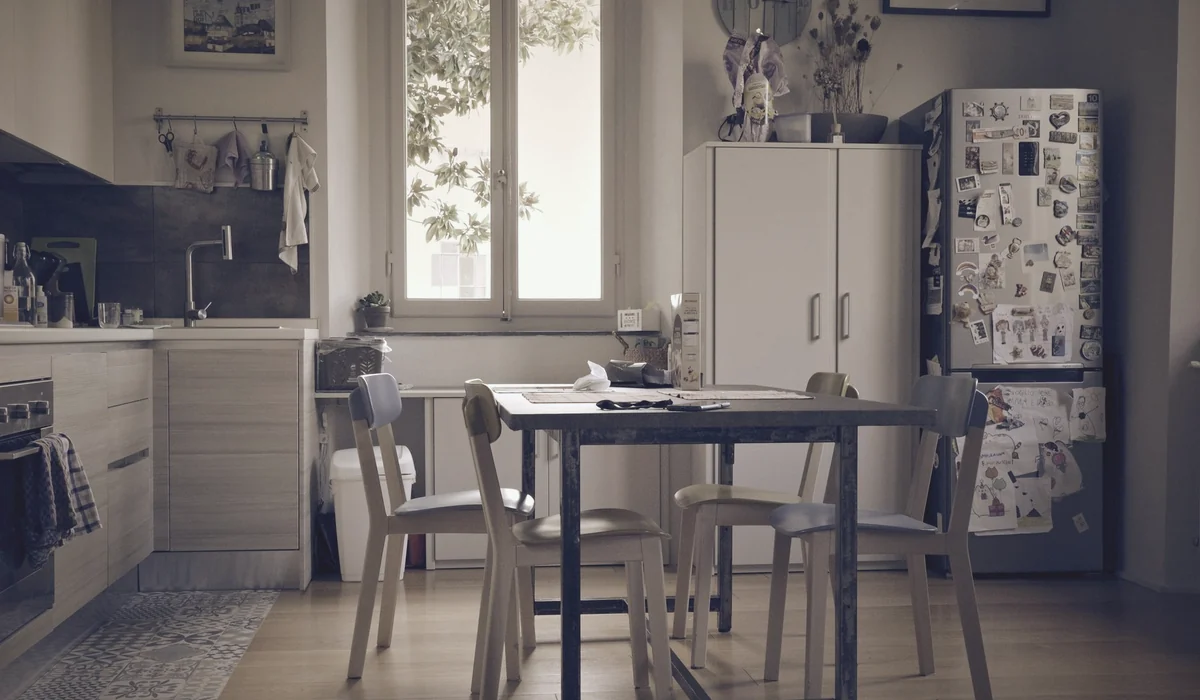 A bright, minimalist kitchen with a vintage table and chairs under natural light from a window.