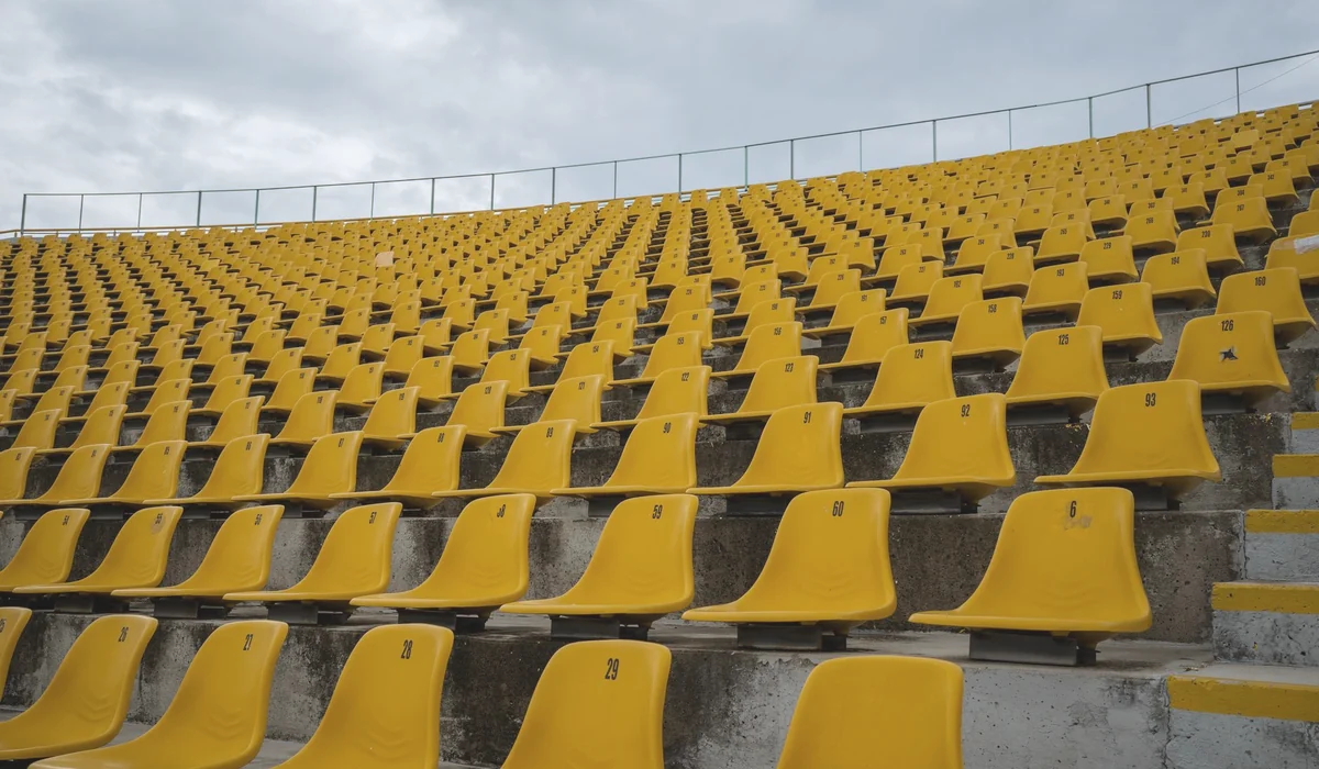 View of empty yellow seats arranged in rows at a stadium on a cloudy day.