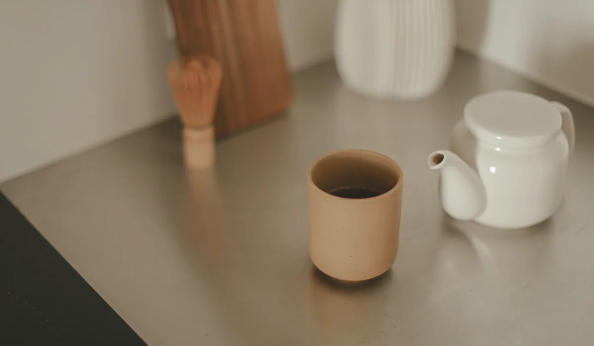 Minimalist kitchen scene featuring a teapot and a ceramic cup on a counter.