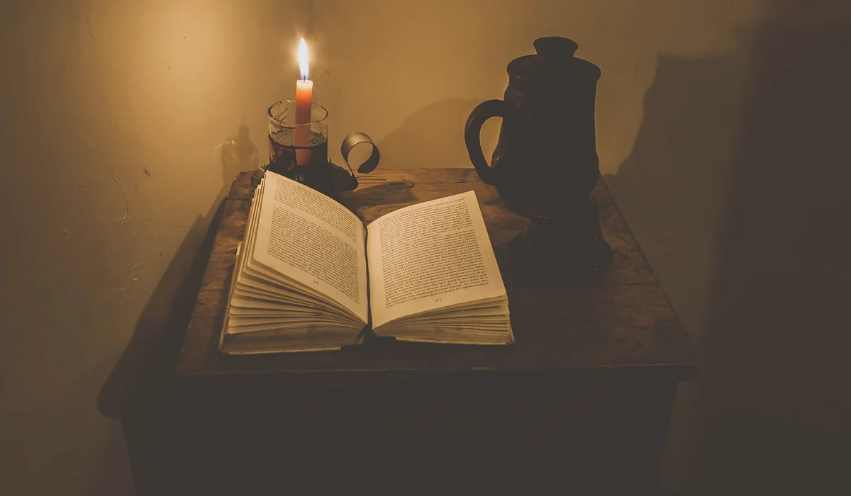 A warm, atmospheric scene of an open book by candlelight on a wooden table with a dark vase, creating a tranquil reading nook.