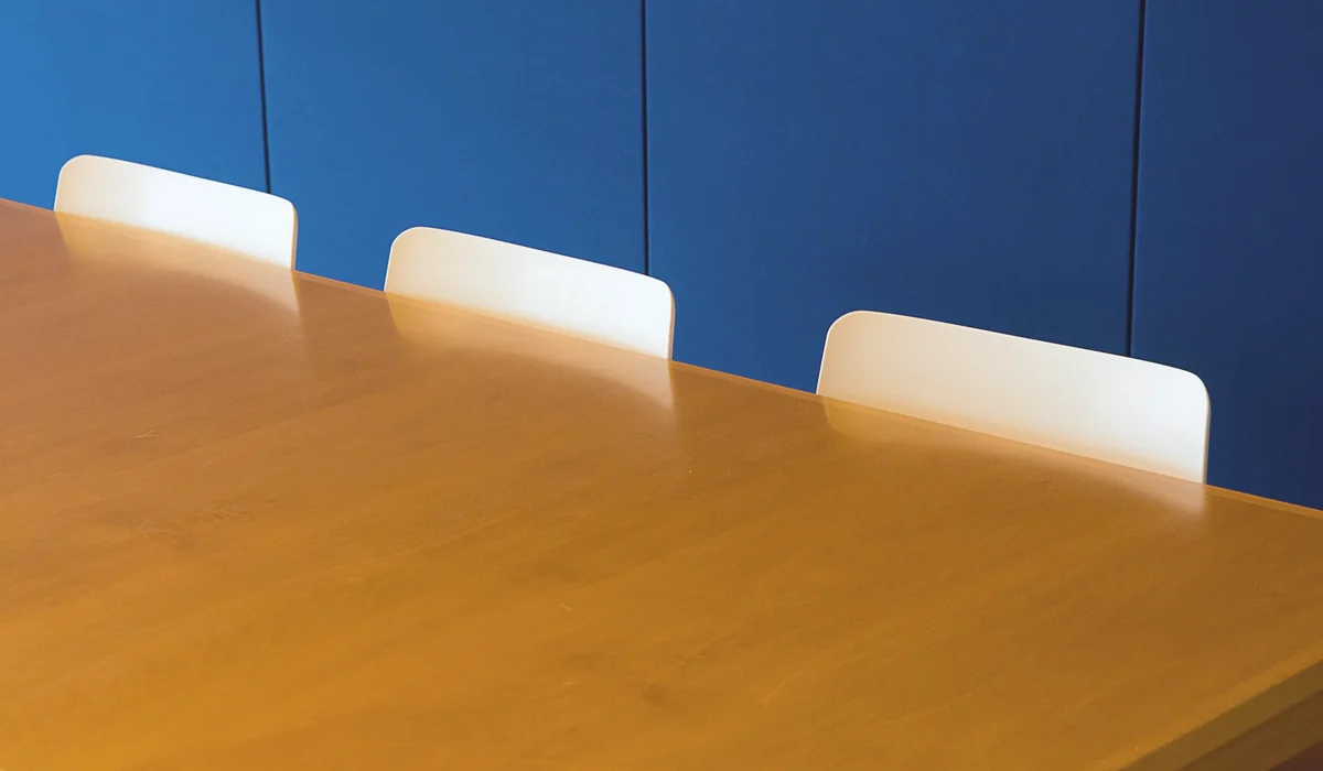 A clean and modern indoor meeting room with a wooden table against a blue wall.