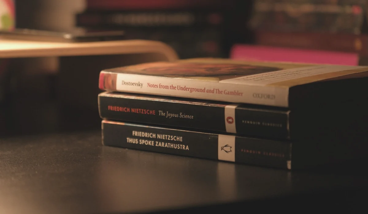 Stack of classic books by Dostoevsky and Nietzsche on a dark desk.