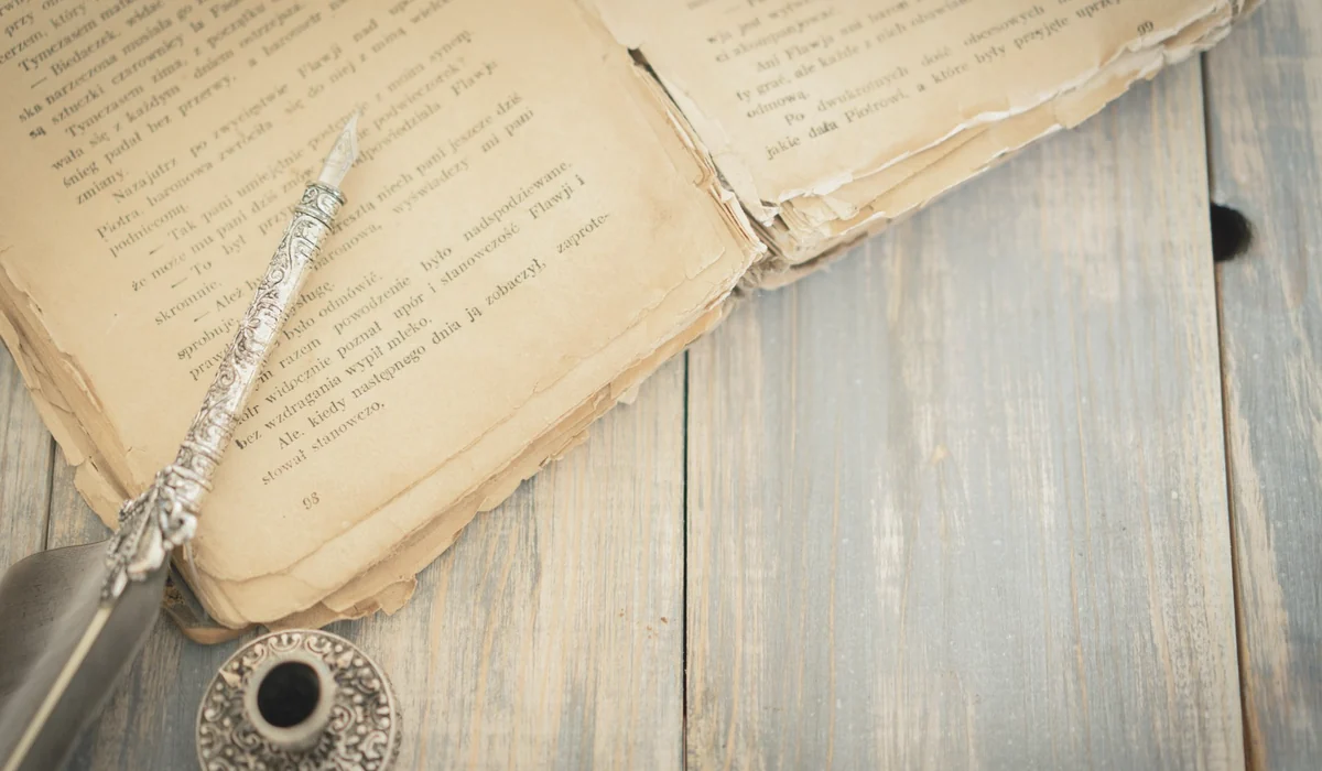 Close-up of an antique book with an ornate quill and ink pot on a wooden surface, evoking a classic vintage feel.