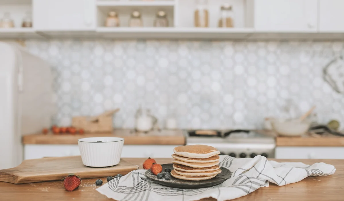 Cozy kitchen scene with pancakes, blueberries, and strawberries on a wooden table.