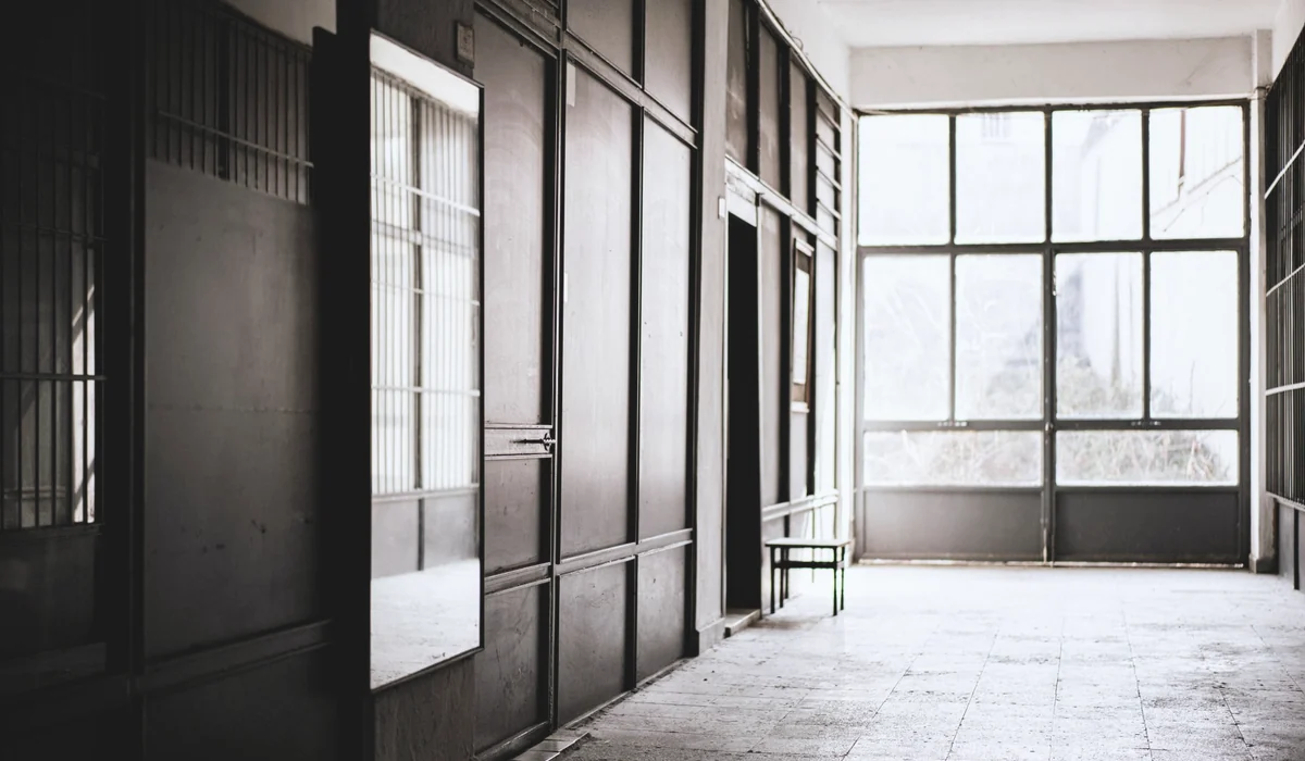 A minimalist industrial hallway featuring large glass windows, abundant light, and muted tones.