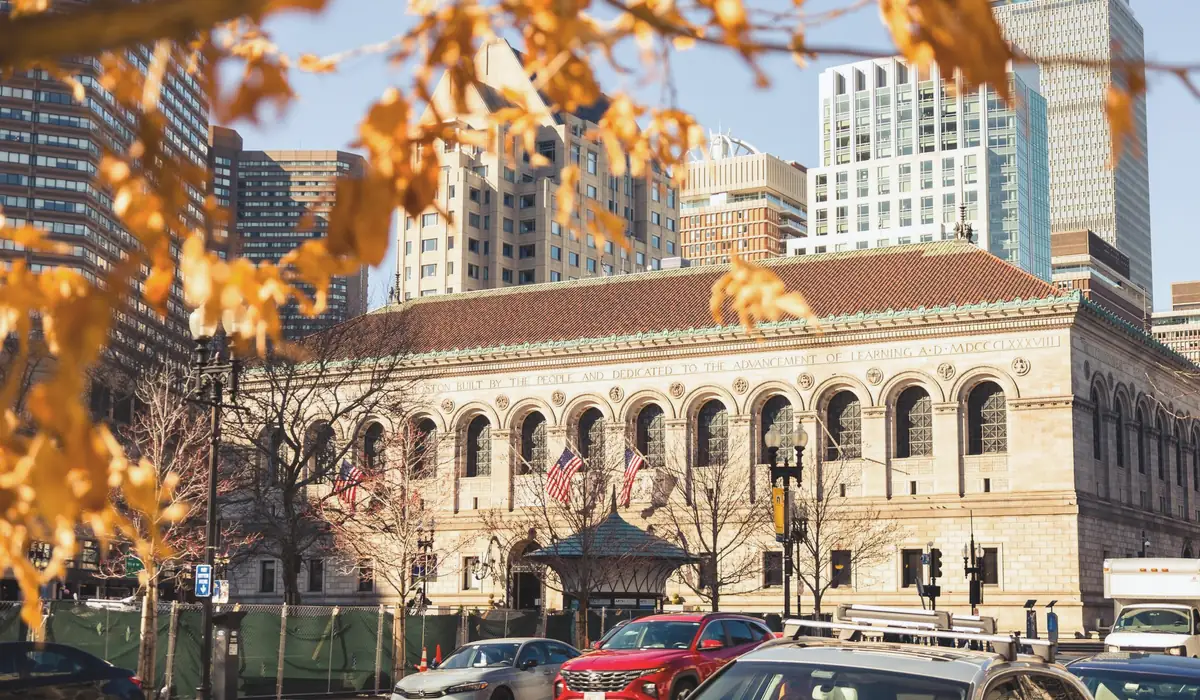 Historic Boston Public Library framed by autumn leaves in vibrant downtown cityscape.