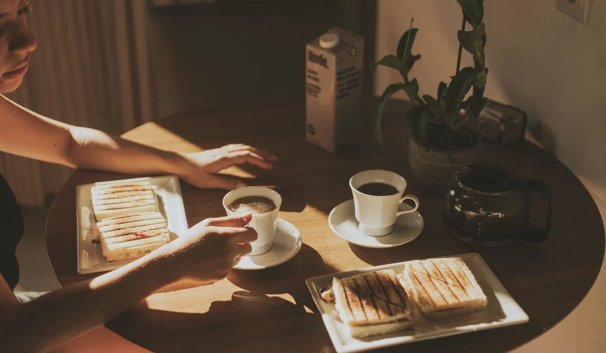 Warm morning light on coffee and grilled sandwiches in a cozy indoor setting.