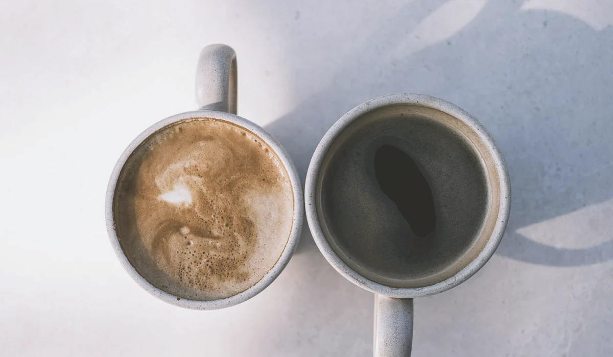 Aerial view of two coffee cups casting shadows on a sunny table, showcasing latte and black coffee.