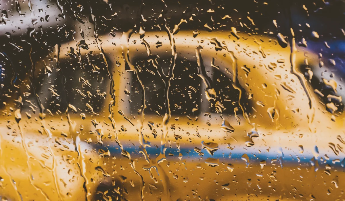Blurred view of a yellow taxi through a rain-soaked window in Kolkata, India.