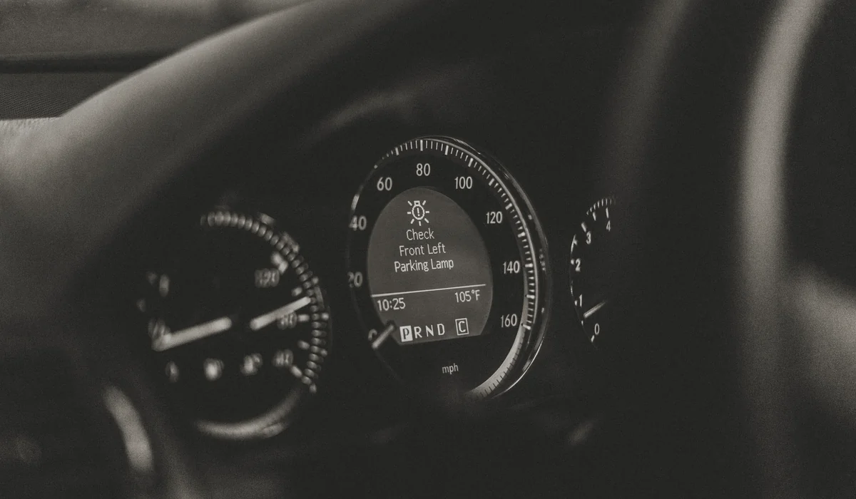 Close-up of a car dashboard in black and white with a parking lamp warning light.