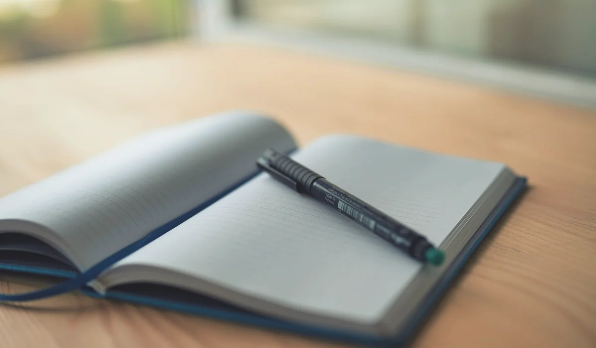 An open lined notebook with a pen resting on a wooden desk, capturing a moment of creativity.