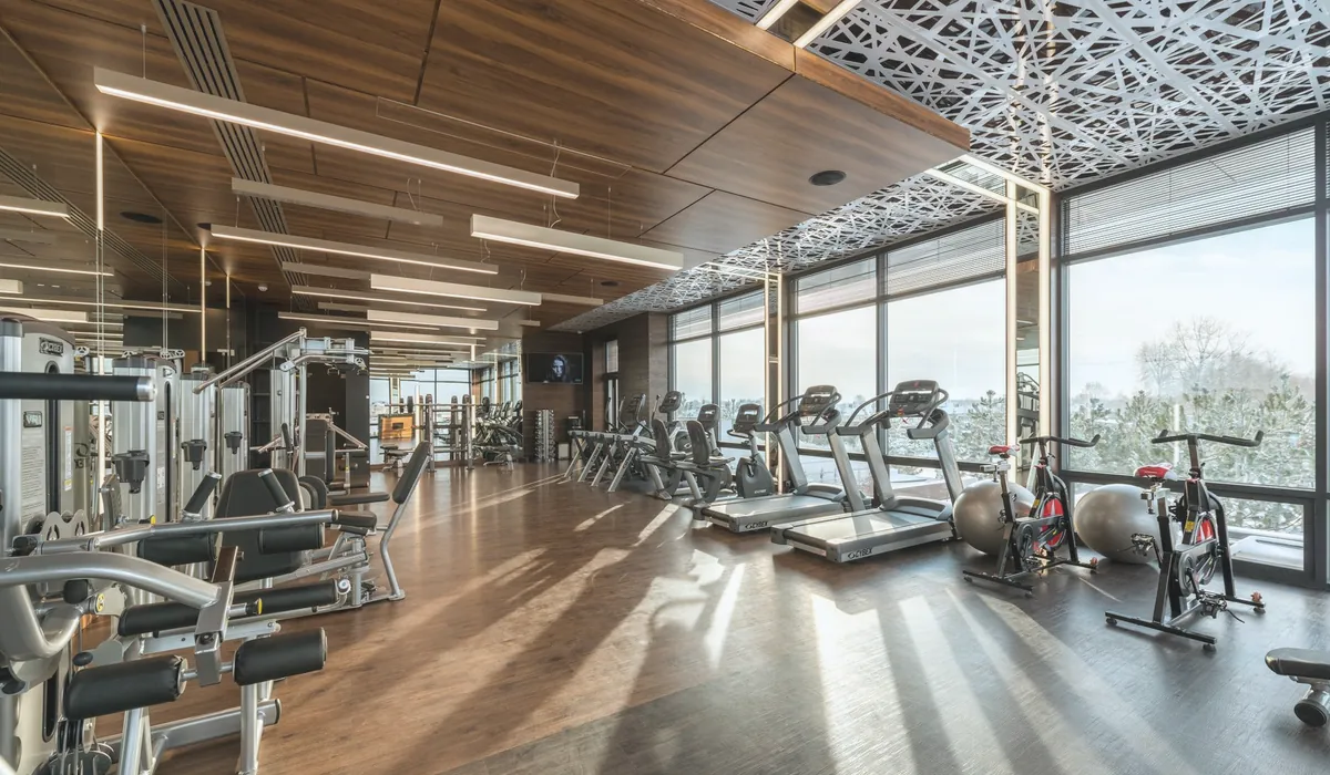 Modern exercise bikes and treadmills and various fitness equipment in spacious gym with wooden floor and panoramic windows in sunlight