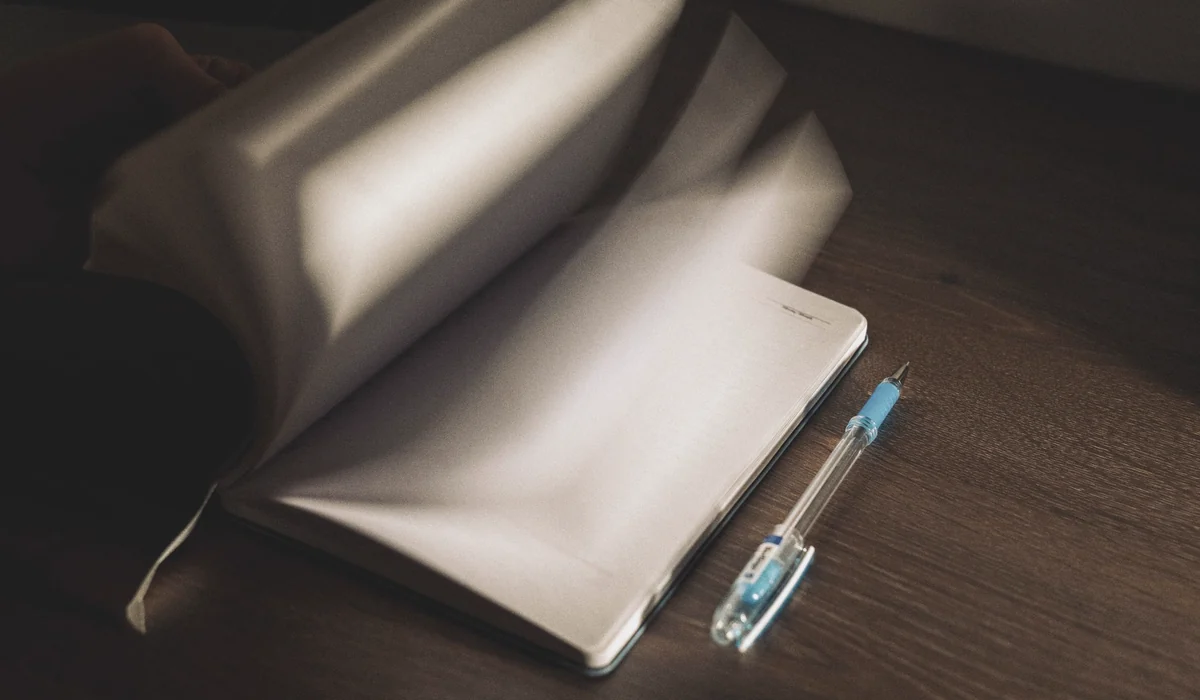 A notebook with turning pages and a pen on a wooden desk in low light.