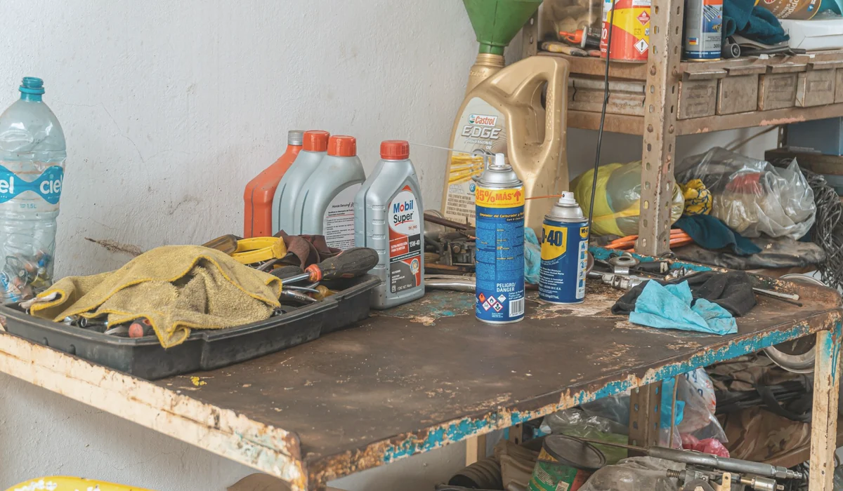 A cluttered workbench in an automobile garage with tools, oil cans, and maintenance products.