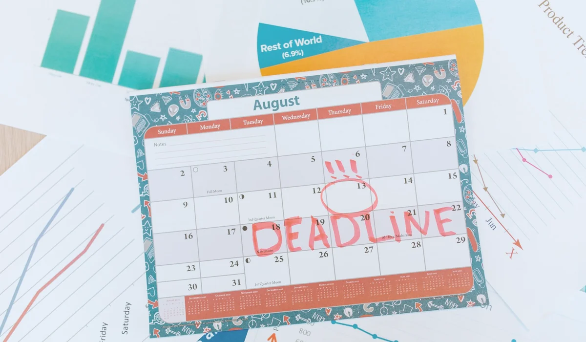 Vibrant August calendar on a desk with deadline marked in red, surrounded by graphs and charts.