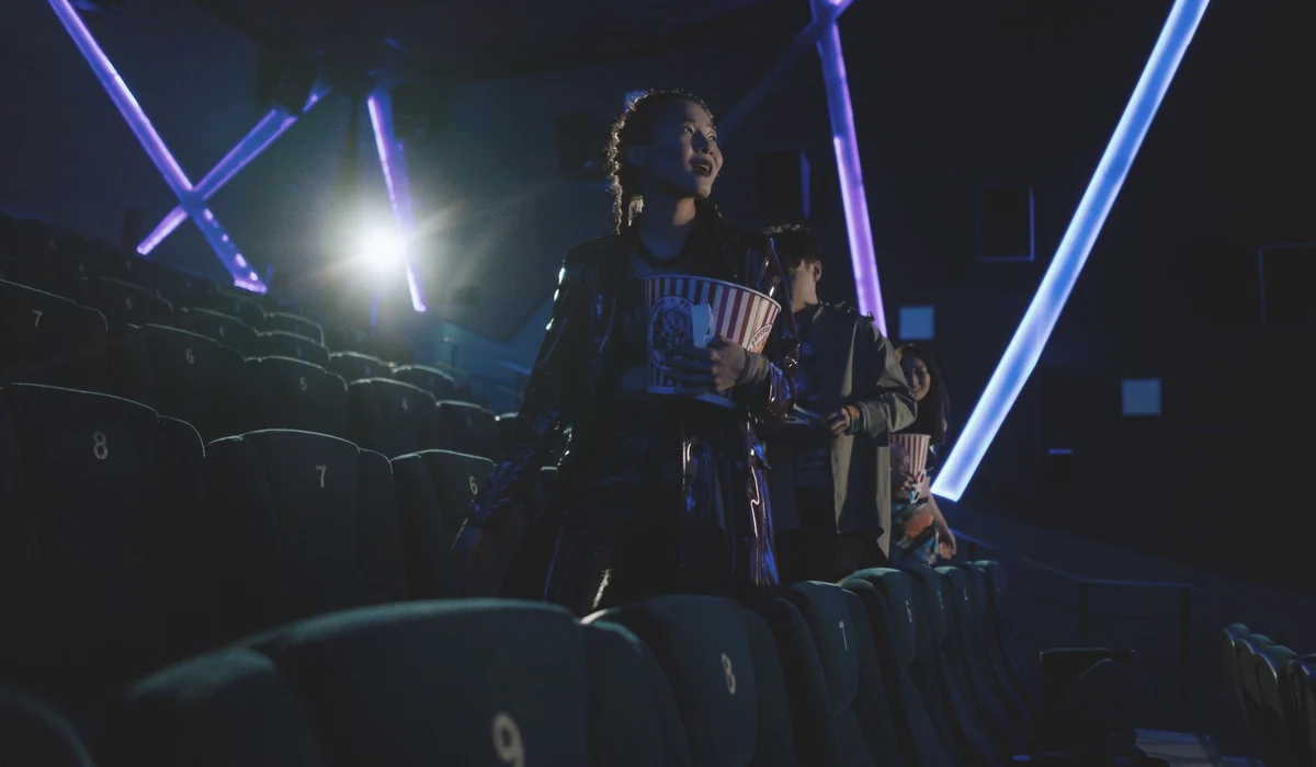 Young adults enjoying popcorn in a private cinema with neon lights.
