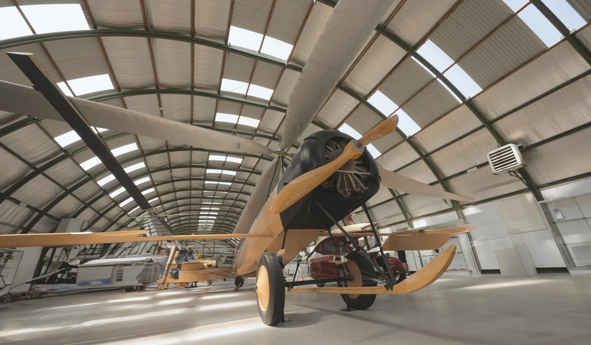 A vintage aircraft displayed in a hangar with an arched roof structure, showcasing aviation history.