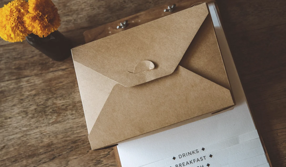 Brown envelope and clipboard on a wooden table with marigold flowers, offering a vintage and cozy ambiance.